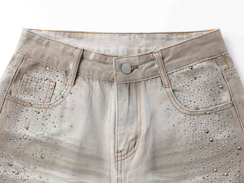 Close-up of the front waistband on washed denim pants with button closure and rhinestone details