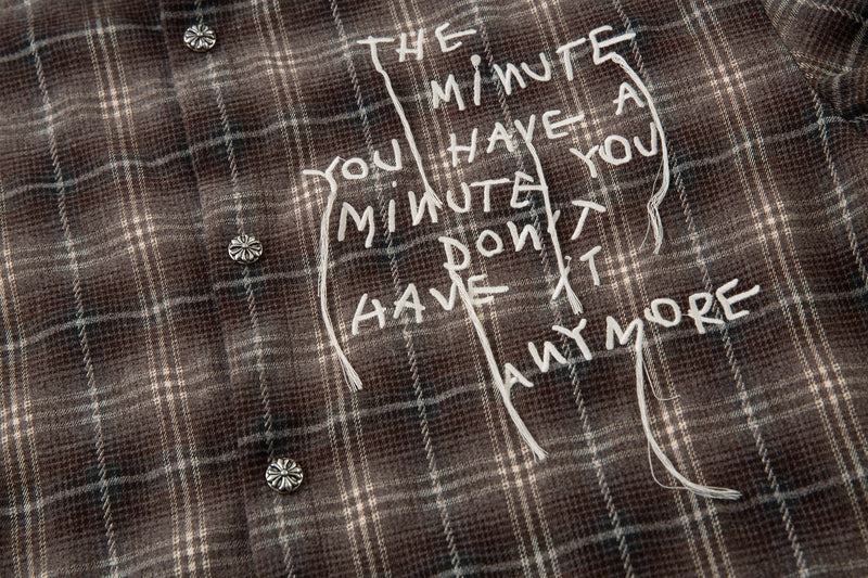 Front close-up of brown plaid shirt with white graphic text and button placket