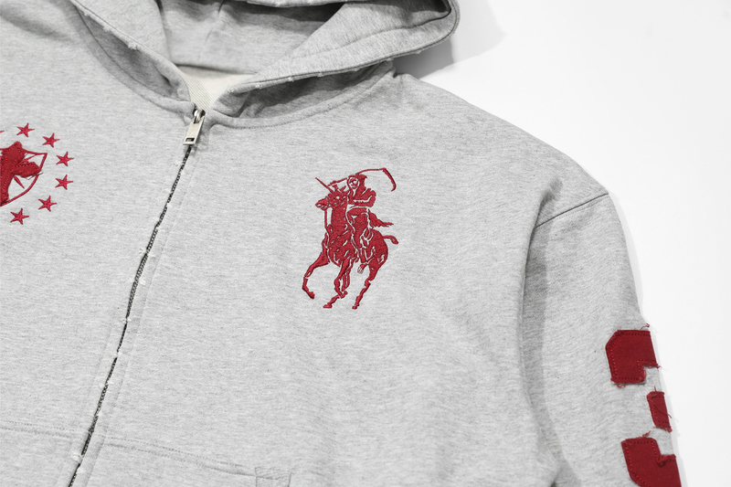 Close-up of light gray hoodie chest showing red rider embroidery and sleeve patch edge