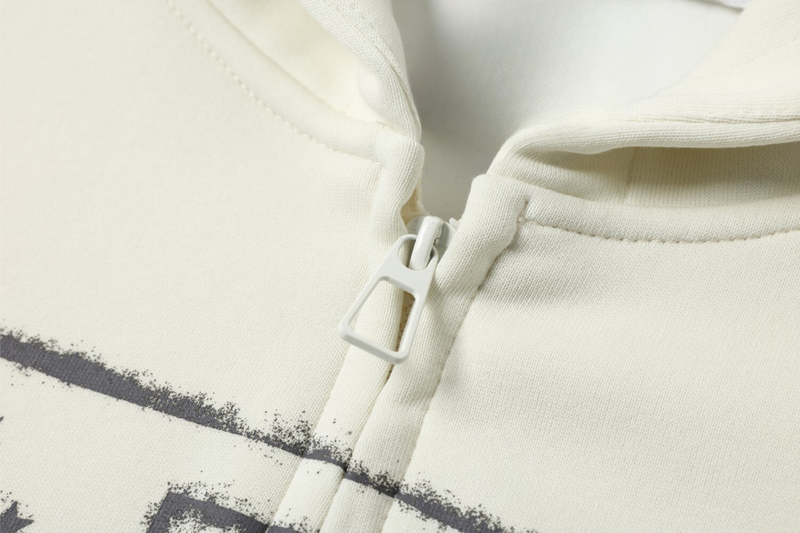 Close-up of cream zip-up hoodie front zipper and printed chest graphic edge