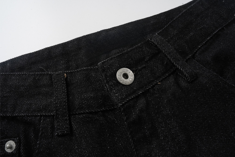 Close-up of black denim waistband with front button, belt loop, and pocket seam