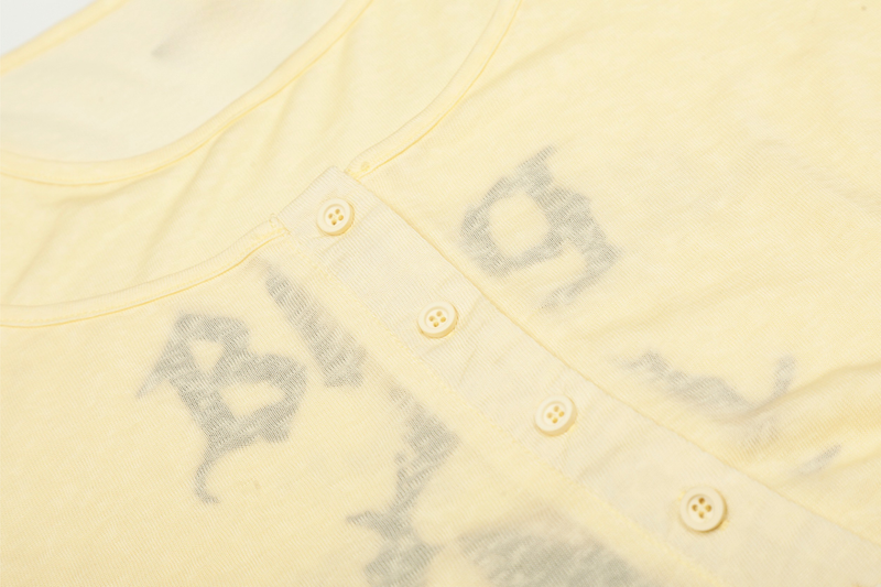 Close-up of light yellow Henley placket with buttons and faded print beneath