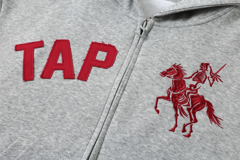 Close-up of red TAP lettering and skeleton rider embroidery on light gray hoodie