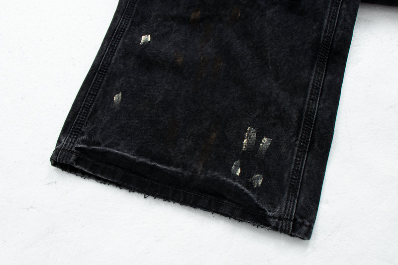 Close-up of black denim hem with distressed paint marks and frayed edge