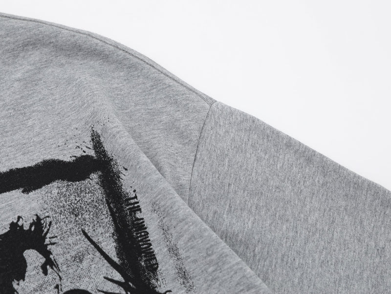 Close-up of a gray oversized graphic tee with black abstract portrait print and visible shoulder seam on a white background