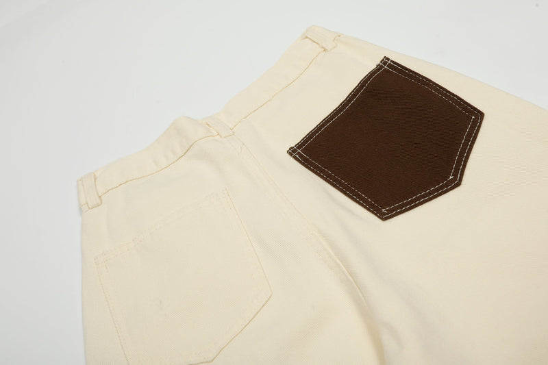 Close-up of cream pants back pocket with brown contrast patch and topstitching