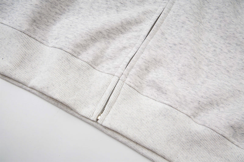 Close-up of the light gray hoodie hem with ribbed trim and zipper edge
