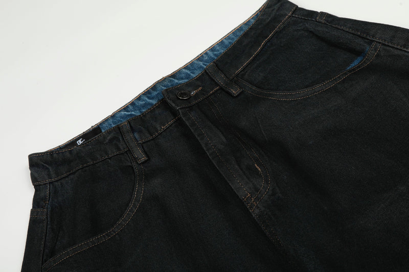Close-up of black denim waistband and front pocket with contrast stitching and blue inner trim