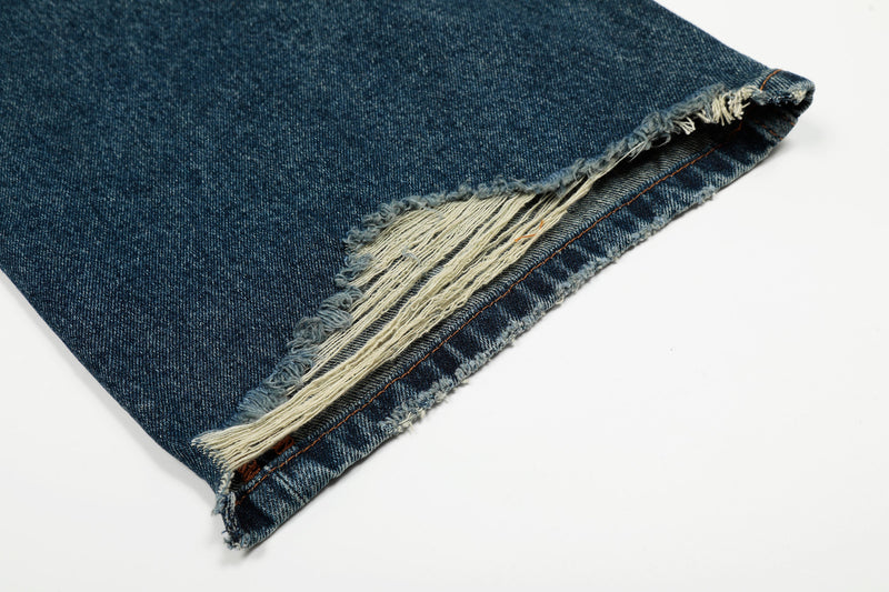 Torn hem close-up with exposed white threads on vintage wash denim