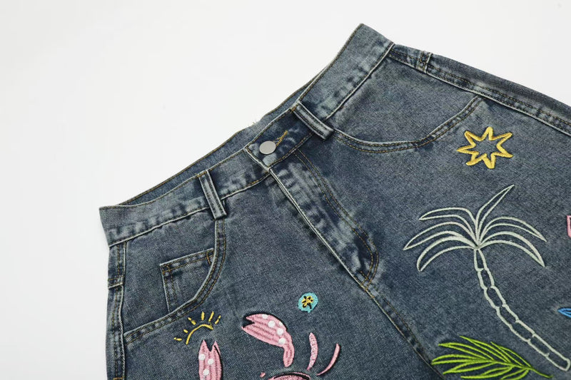 Close-up of front waistband, pocket and tropical embroidery on blue denim jeans
