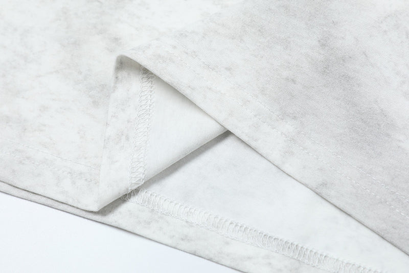 Close-up of white tie-dye graphic tee fabric with visible hem stitching and soft streetwear texture