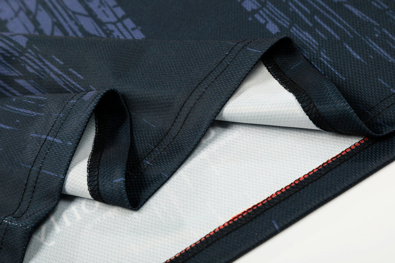 Close-up of a dark mesh soccer jersey with folded sleeves, blue pattern details, and red stitched hem trim