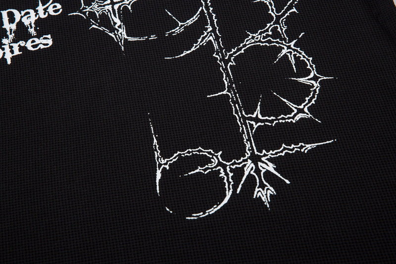Close-up of black textured polo shirt with white thorny Gothic cross graphic and distressed streetwear lettering