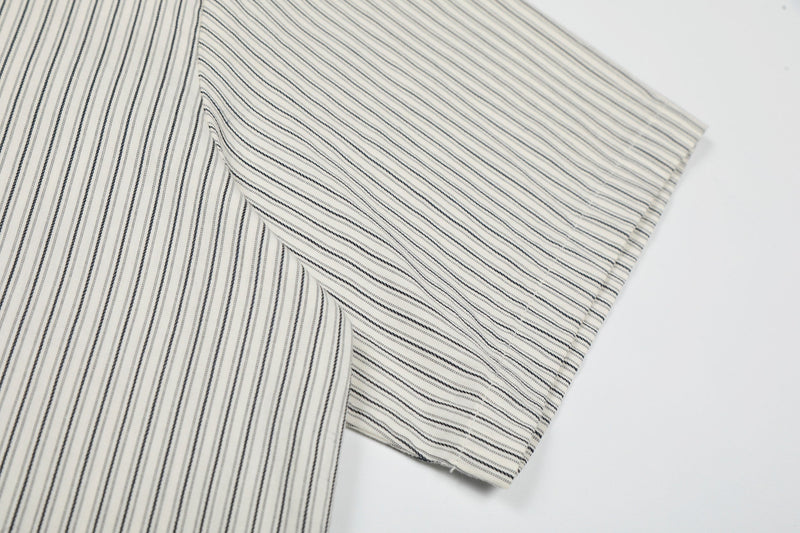 Cream pinstripe button-up shirt with black patch details and relaxed streetwear styling on a white background
