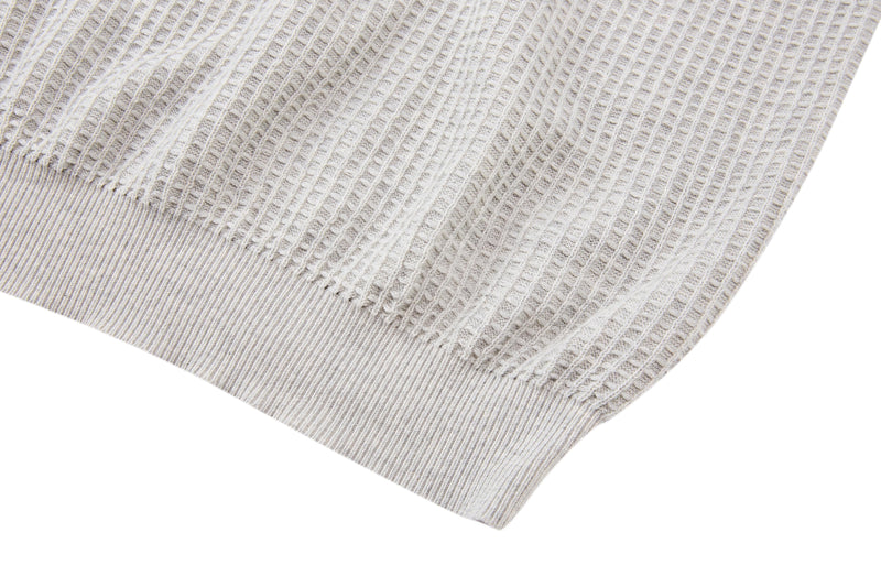 Close-up of a light beige waffle knit short-sleeve sweater hem with ribbed trim and textured cotton blend fabric
