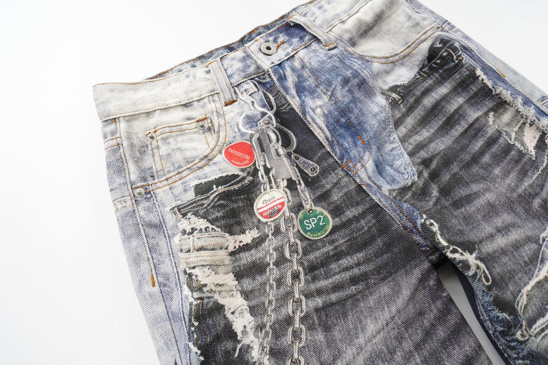 Angled close-up of the front waist on distressed patchwork jeans with chain and graphic print