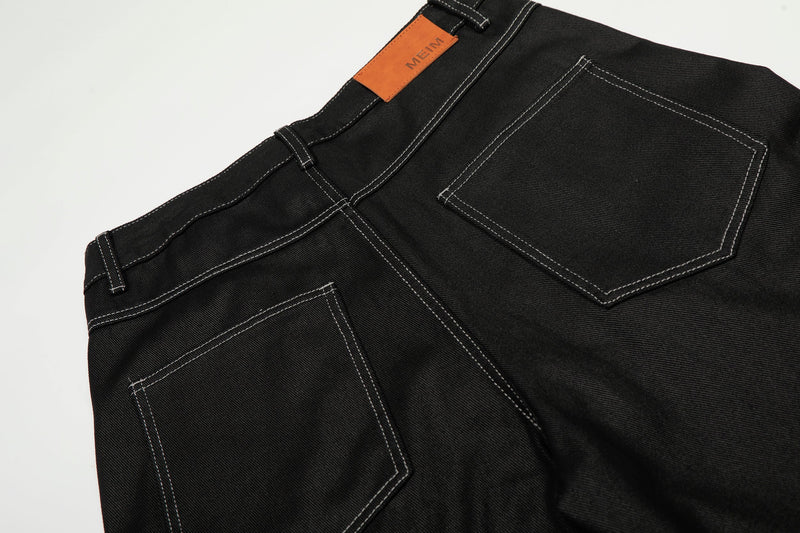 Close-up of the back waistband and pocket on black denim pants with orange logo patch