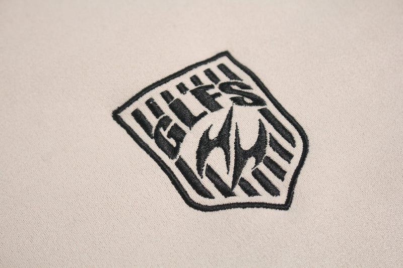 Close-up of a cream Seakoff sport tee with a black embroidered shield logo and bold graphic lettering