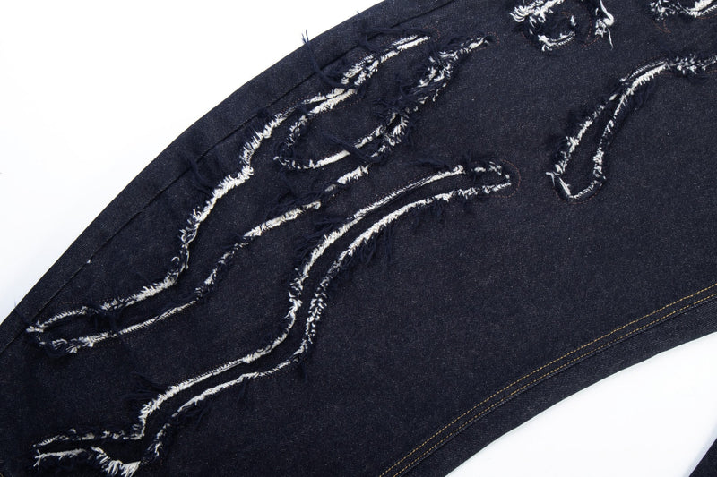 Diagonal close-up of flame-shaped distressing and frayed white stitching on dark jeans leg
