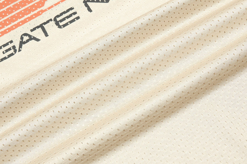 Close-up of cream mesh jersey fabric with orange and black Starline graphic detailing and breathable perforated texture