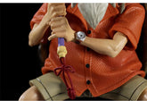 A close-up of the Master Roshi Collectible Figure with Banana Fan by Seakoff, featuring intricate detailing in its orange textured shirt and beige shorts. The figure holds a staff and sports a wristwatch, while the dark background highlights these features.