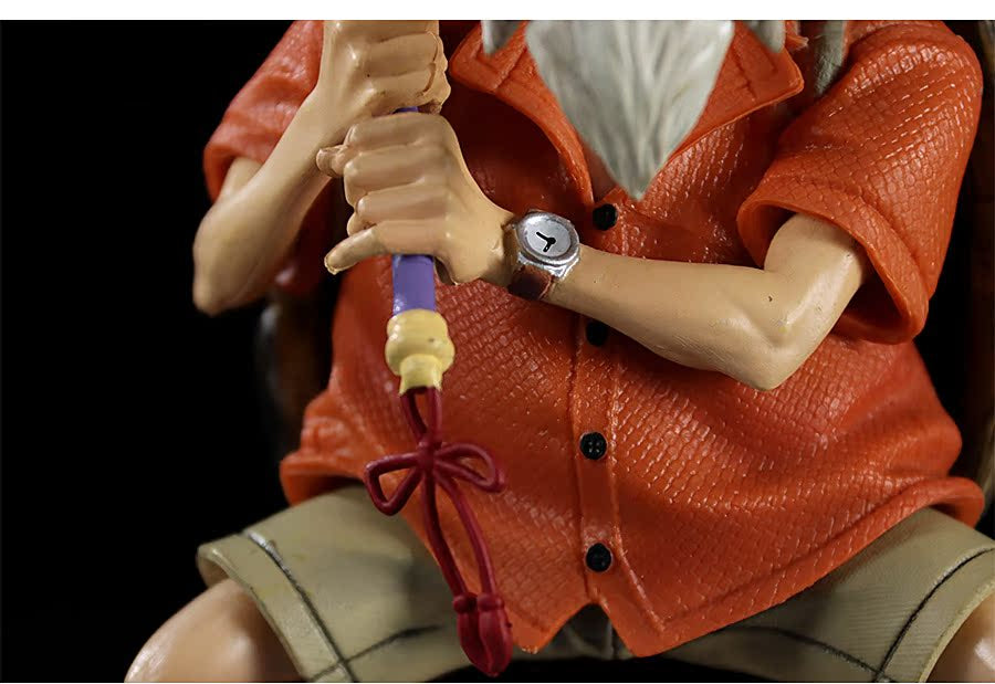 A close-up of the Master Roshi Collectible Figure with Banana Fan by Seakoff, featuring intricate detailing in its orange textured shirt and beige shorts. The figure holds a staff and sports a wristwatch, while the dark background highlights these features.