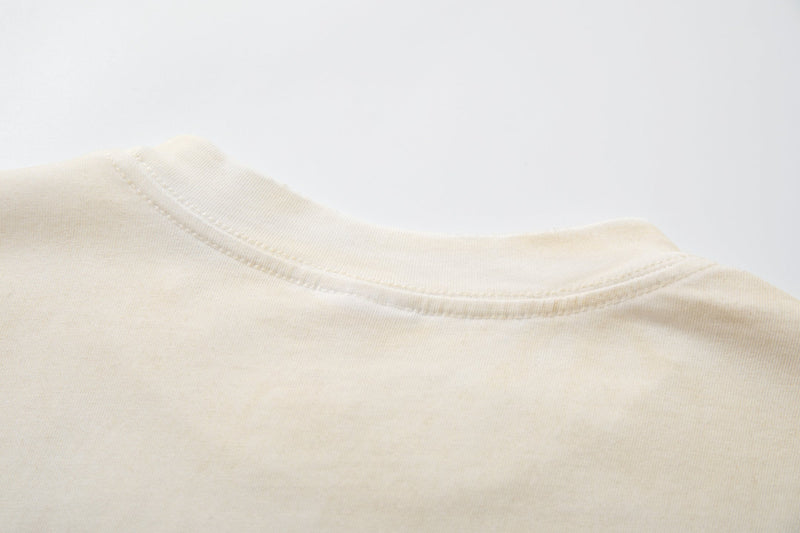Close-up of a cream retro streetwear graphic tee neckline with visible stitching and soft cotton fabric texture