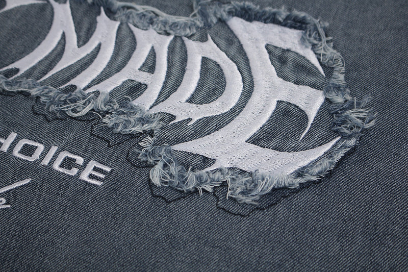 Close-up of a vintage washed black graphic T-shirt with frayed white distressed lettering on denim-textured fabric