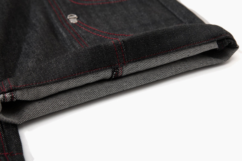 Close-up of folded black denim hem showing inner light-colored cuff and red stitching