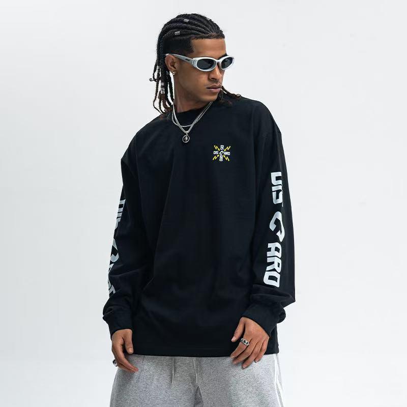 Black long sleeve tee with small chest graphic and bold white sleeve print, worn on model