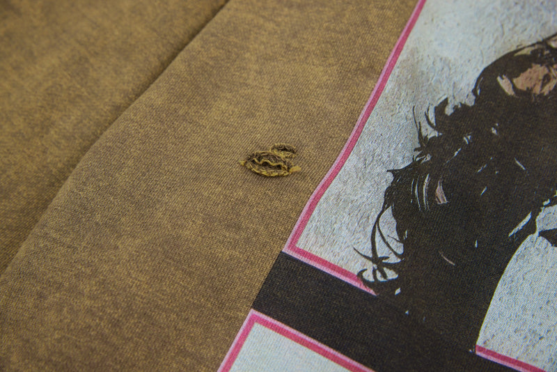 Close-up of distressed hole next to front graphic on brown tee