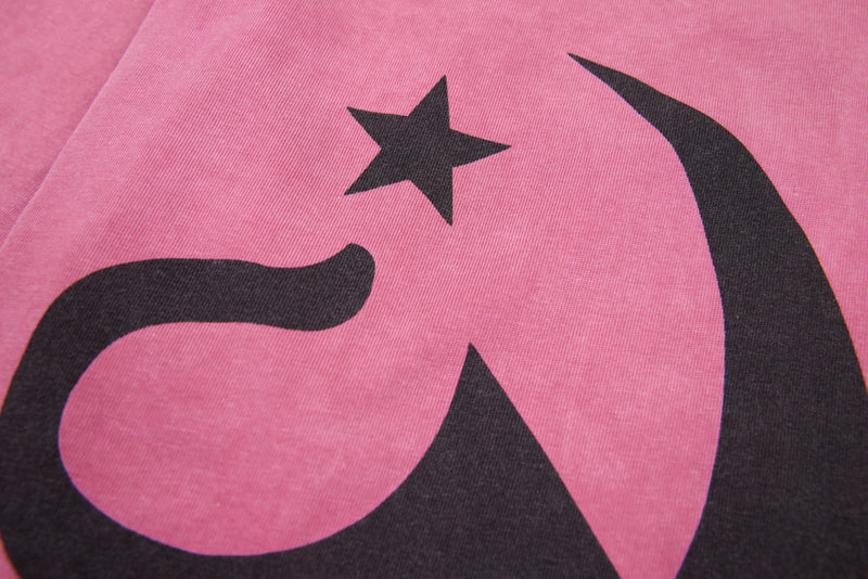Close-up of black star and curved graphic on pink graphic tee front