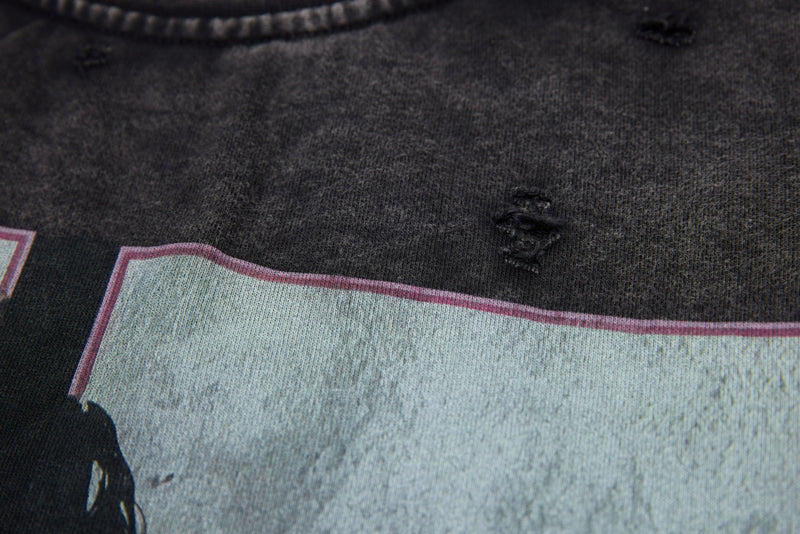 Front chest close-up of black washed tee showing distressed hole details and print edge