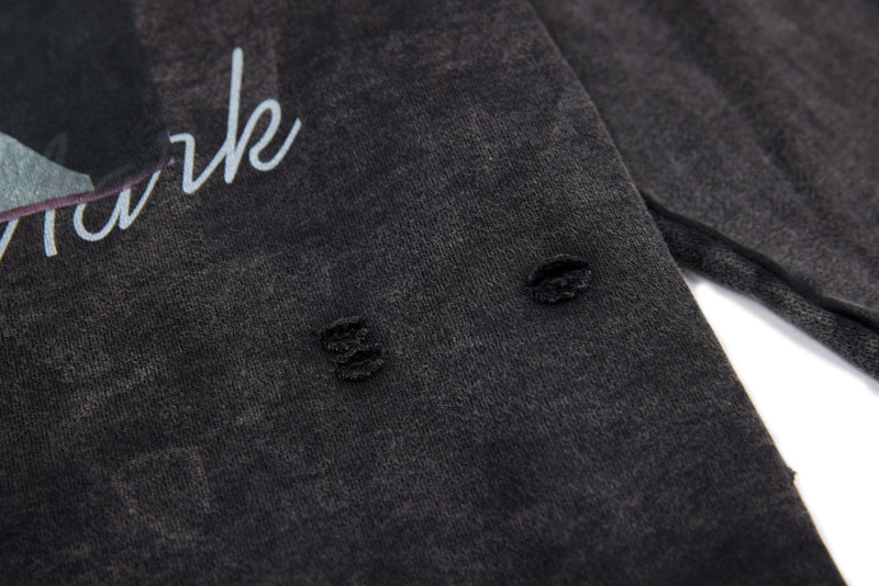Black washed tee sleeve close-up with distressed holes and partial script print