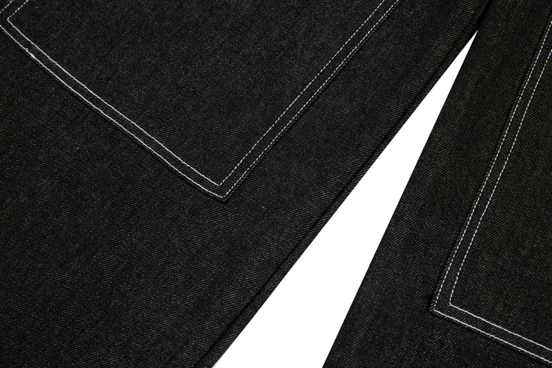 Close-up of black denim legs with angled panel seams and white stitching