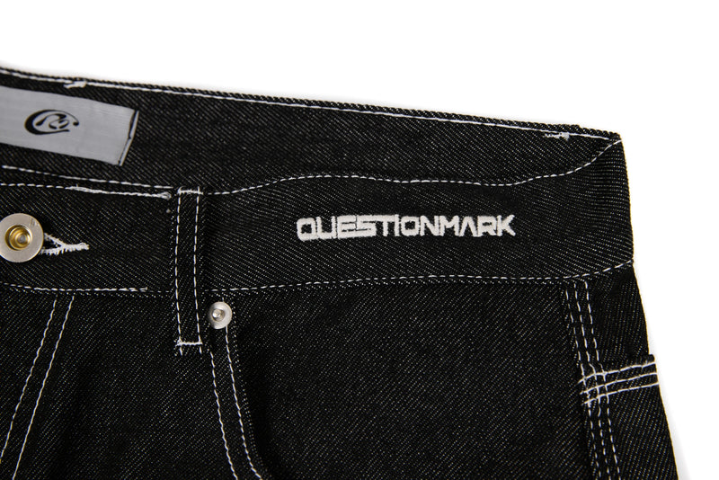 Close-up of black denim waistband showing Questionmark embroidery and front button detail