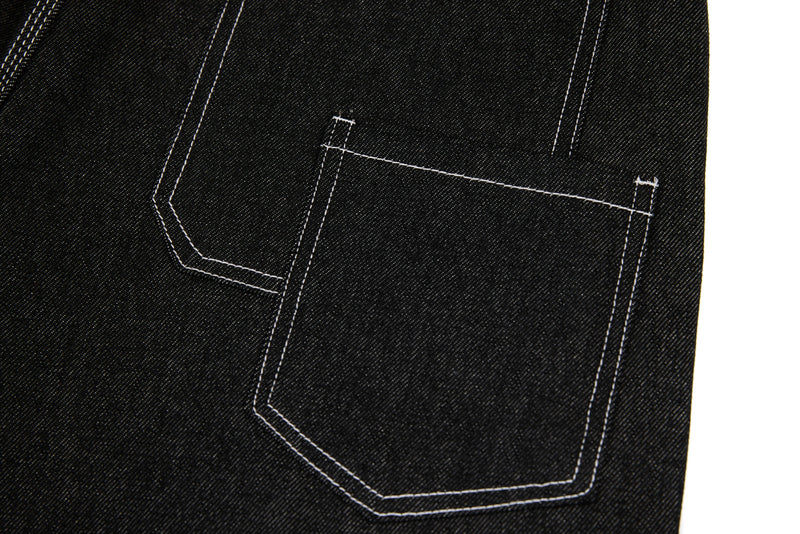 Close-up of black denim back pocket with geometric panel stitching and white seams