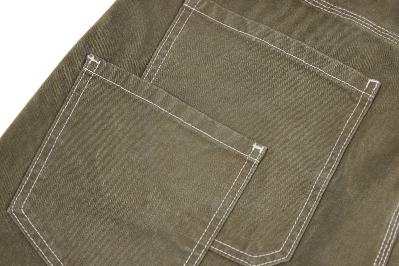 Close-up of olive denim pants back patch pockets with contrast stitching