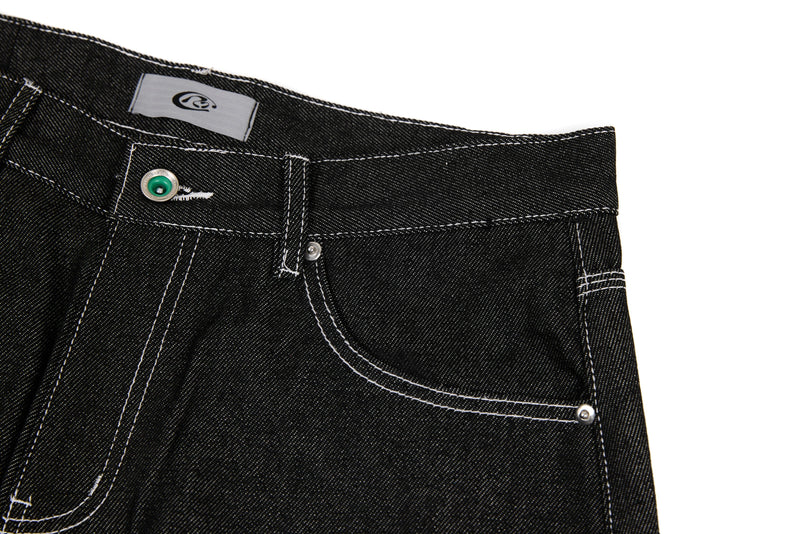 Front waist close-up of black denim jeans with green button and curved pocket seam