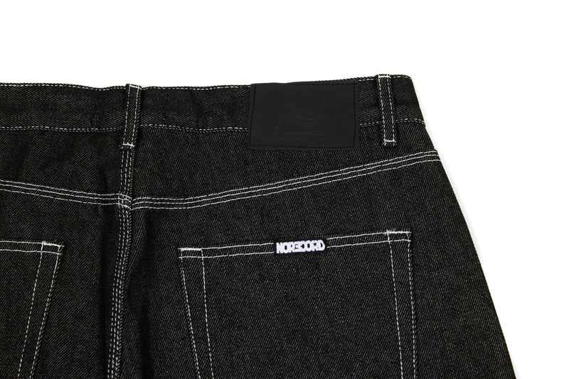 Back waist close-up of black denim jeans with black patch label and stitched pocket