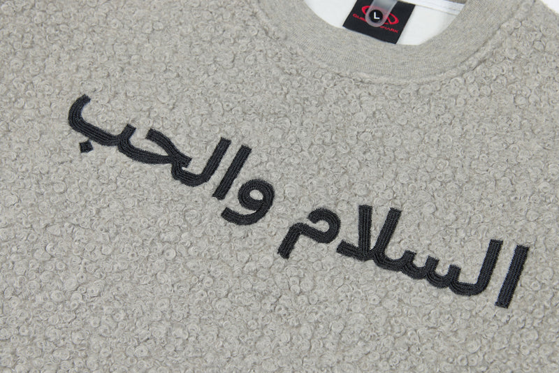 Close-up of light gray sweatshirt front showing black Arabic text embroidery