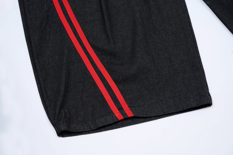 Bottom hem of dark denim pants with twin red side stripes, close-up