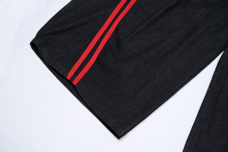 Lower leg of dark denim pants with red side stripes near hem