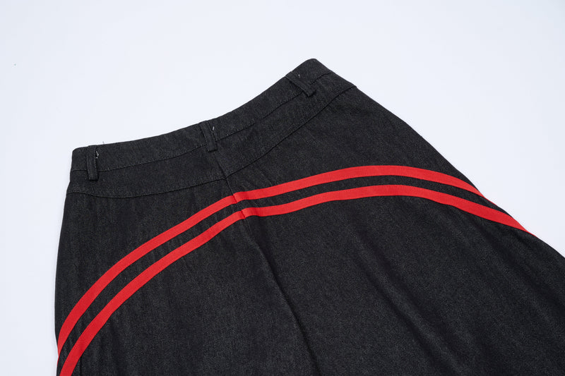 Upper dark denim pants with curved red side stripes, angled view