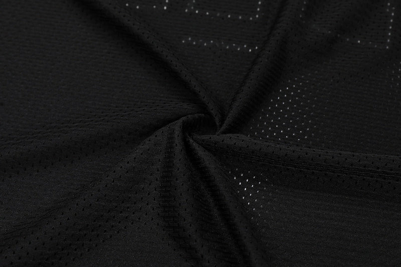 Close-up of black perforated mesh football jersey fabric with textured panels and leather-look detailing