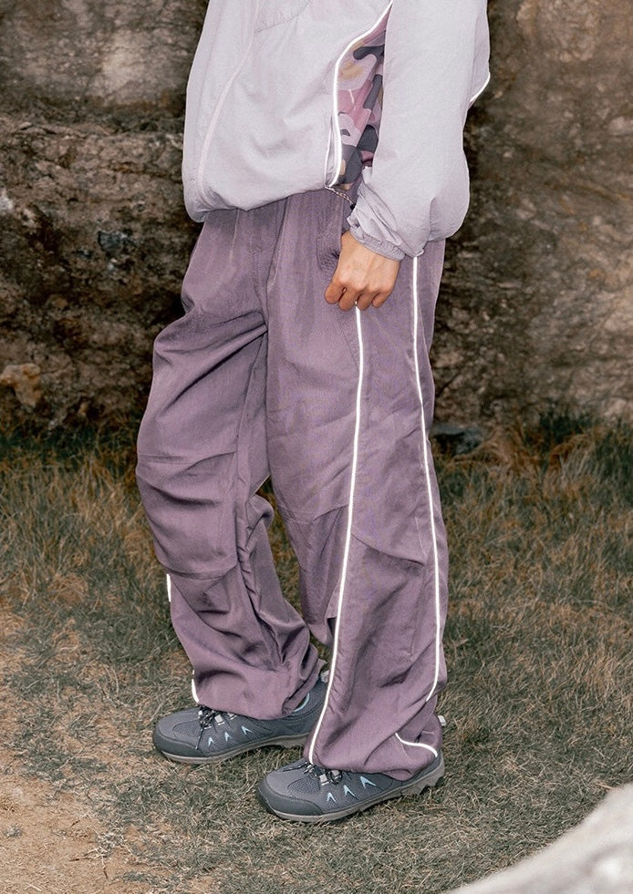 Person wearing relaxed-fit dusty mauve nylon cargo pants with reflective white side piping and grey trail shoes
