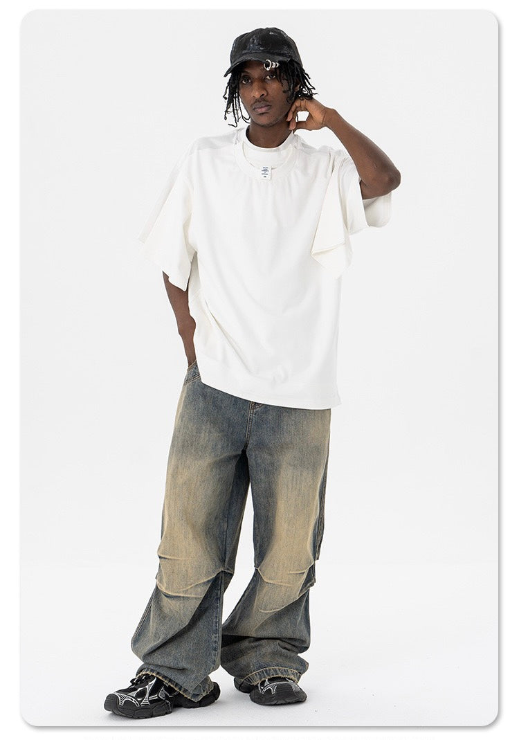 Model wearing oversized white optical illusion T-shirt with layered sleeve detail, baggy faded jeans, and black cap on a white background