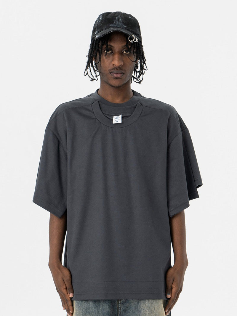 Model wearing a dark gray oversized T-shirt with layered optical illusion sleeves and a loose streetwear fit