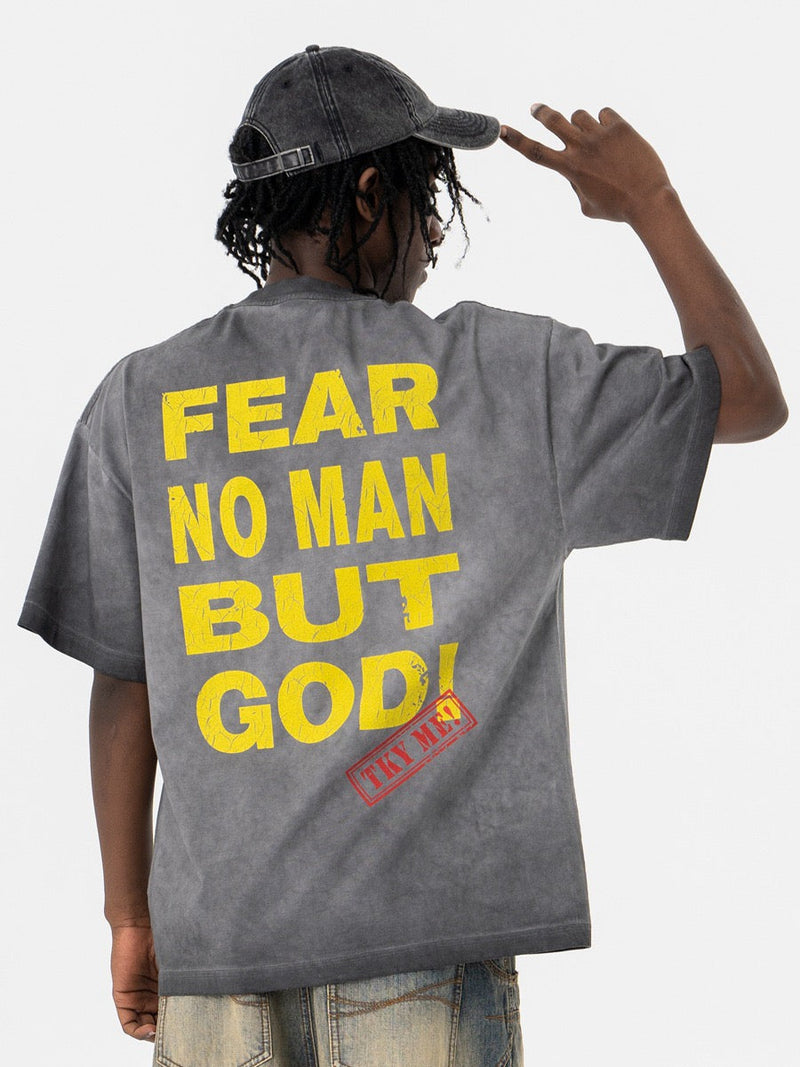 Oversized washed gray graphic tee with yellow Fear No Man But God print on the back, worn with a black cap