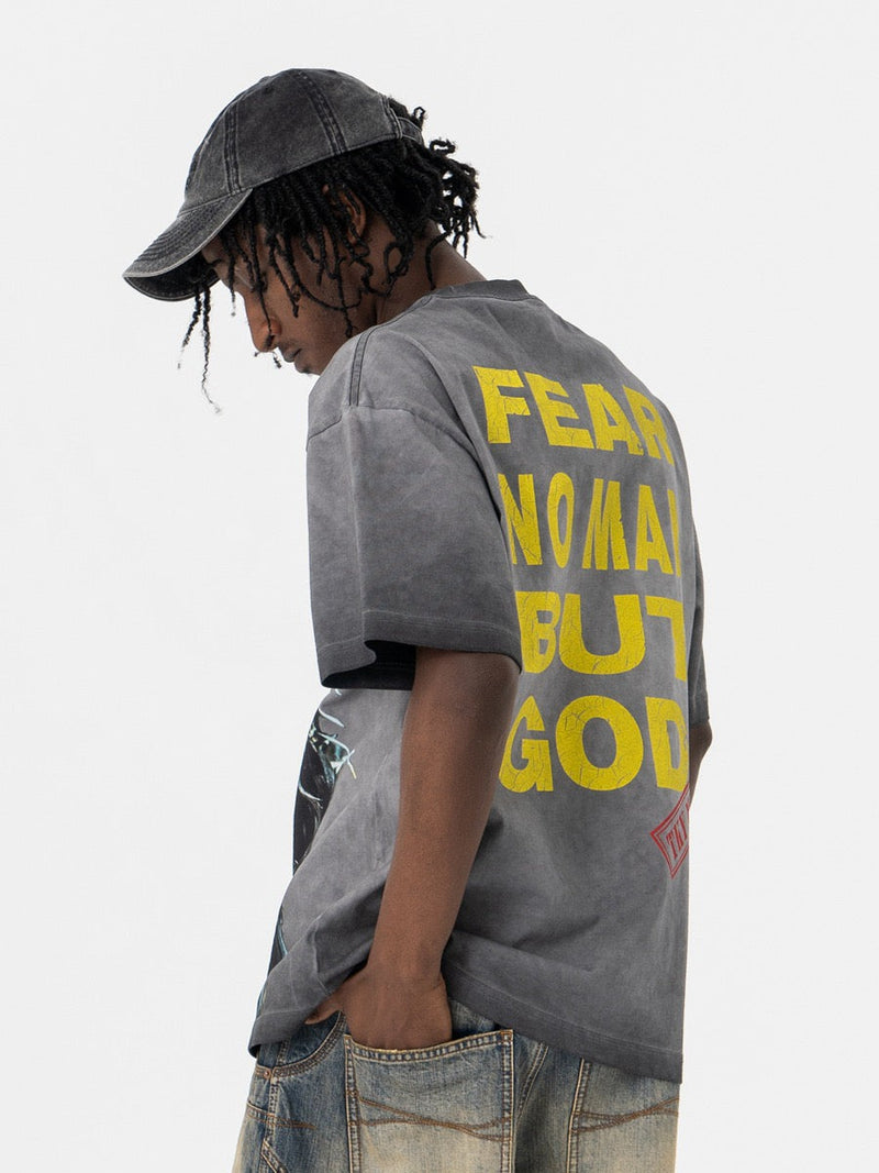 Oversized washed gray graphic tee with yellow back print, worn by a model in a denim cap and patchwork jeans